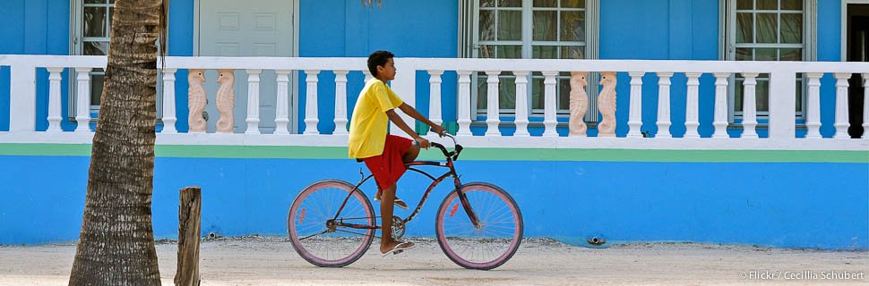 Junge auf Fahrrad vor blauem Haus in Belize